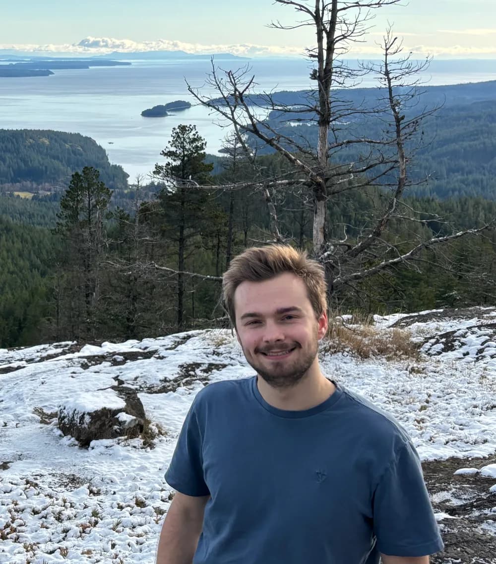 Oliver Kerr, developer of LaneLogic, standing on a snowy viewpoint above a coastal landscape.